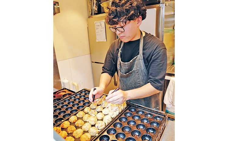 手際良く焼き上げる店長・佐藤翔さん。タコ焼きは海外からの観光客にも人気が高く、8席あるイートイン席は連日賑わいます