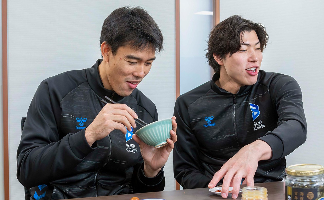 初めて食べる日本の塩辛にも果敢にチャレンジしてくれるバグナス選手。清水選手もやさしくサポート！